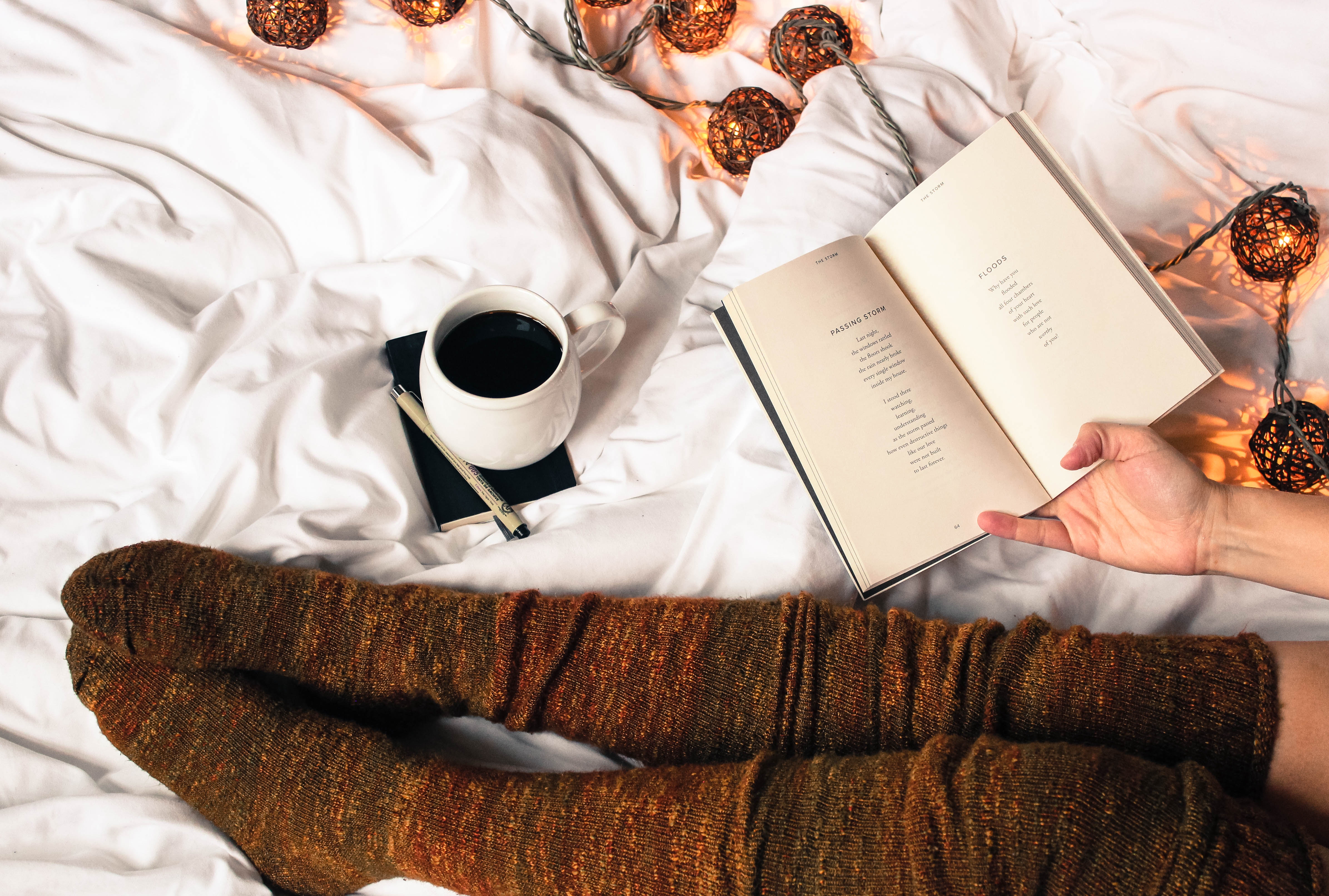 Łóżko na którym siedzi kobieta pijąca kawę i czytająca książke